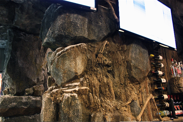 Skeleton embedded in a rock wall decor, adding a unique and mysterious ambiance to the bar interior, ideal for patrons looking for an unforgettable atmosphere.