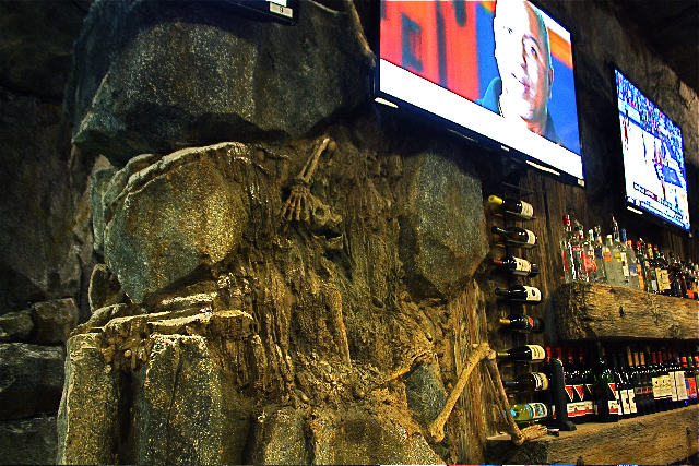 Skeleton embedded in a rock wall decor, adding a unique and mysterious ambiance to the bar interior, ideal for anybody looking to spice up their nightlife
